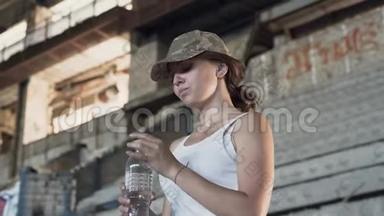 一幅漂亮的年轻女子戴着<strong>军帽</strong>，在尘土飞扬的废弃建筑里喝着瓶子里的水